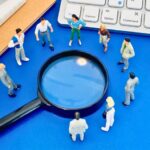 虫眼鏡を囲むミニチュア会社員たち