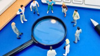 虫眼鏡を囲むミニチュア会社員たち