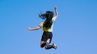 青空背景に元気良くジャンプする女の子