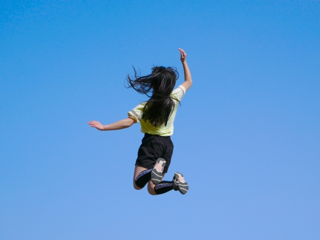 青空背景に元気良くジャンプする女の子