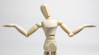 両手を広げて肩をすくめる木製の人形
